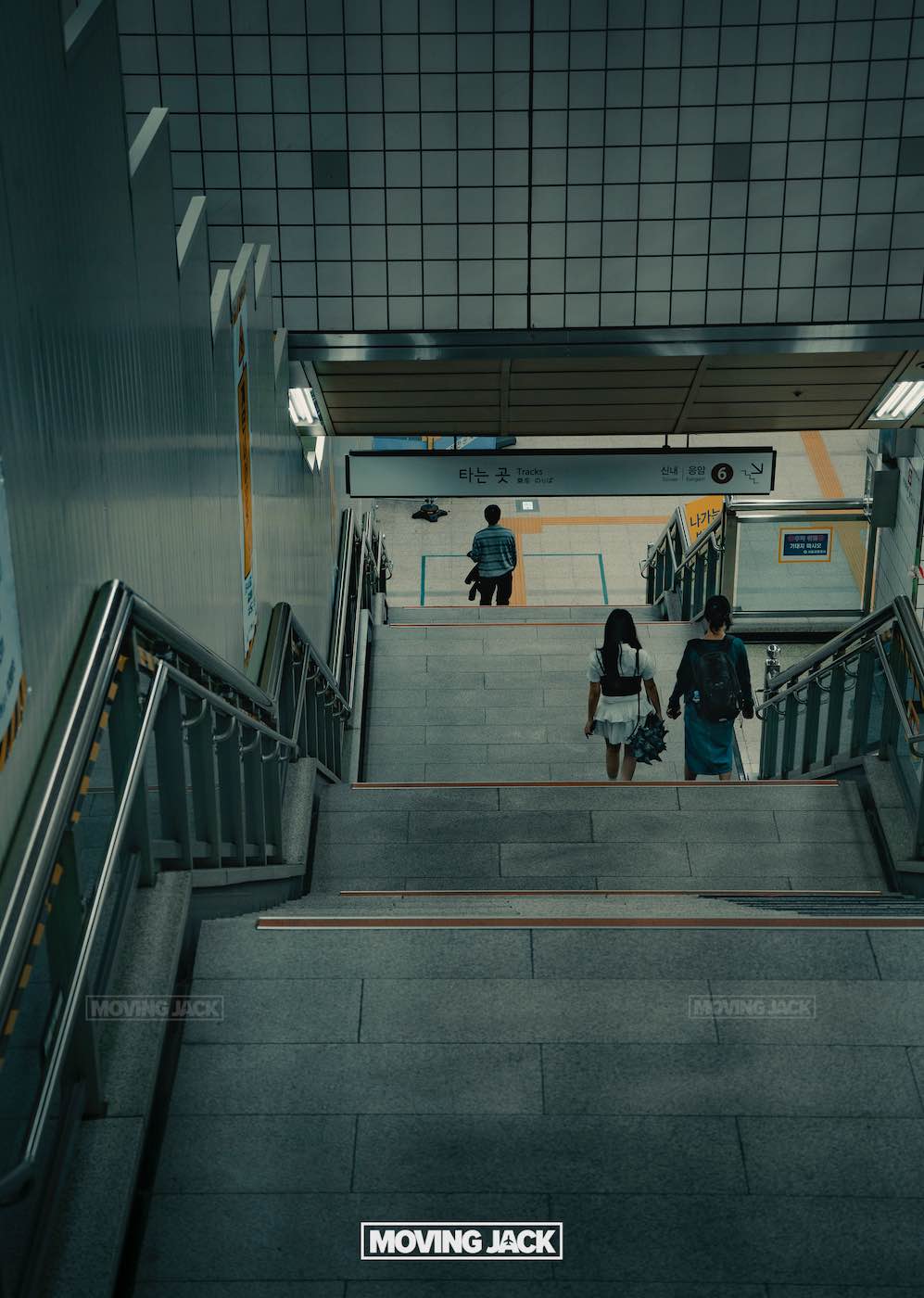 Bezoek Seoul: 12 fascinerende eerste indrukken die je meteen zult herkennen 9 Seoul Drie mensen dalen een trap af naar een betegeld metrostation in Seoul. Twee lopen samen, terwijl één persoon vooruit loopt, vlakbij het perron, en een van de vele gratis activiteiten in Seoul verkent. -copyright-moving-jack.com