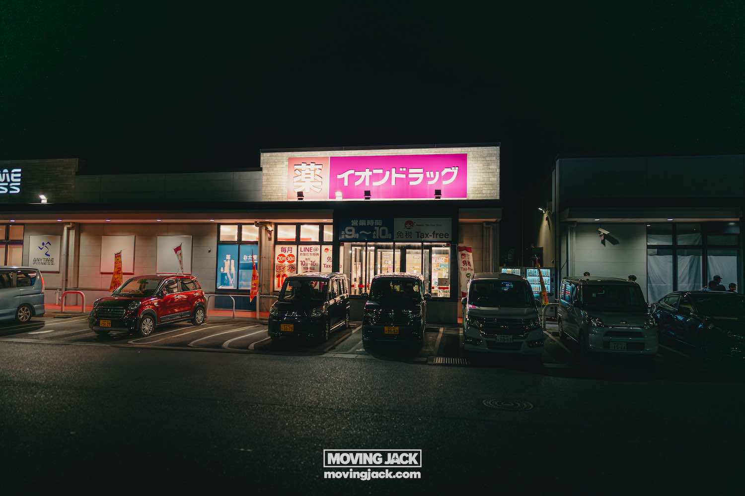 A brightly lit japanese store with a pink sign stands out at night, several cars—perhaps from renting a car in okinawa—parked in front. Copyright-moving-jack. Com