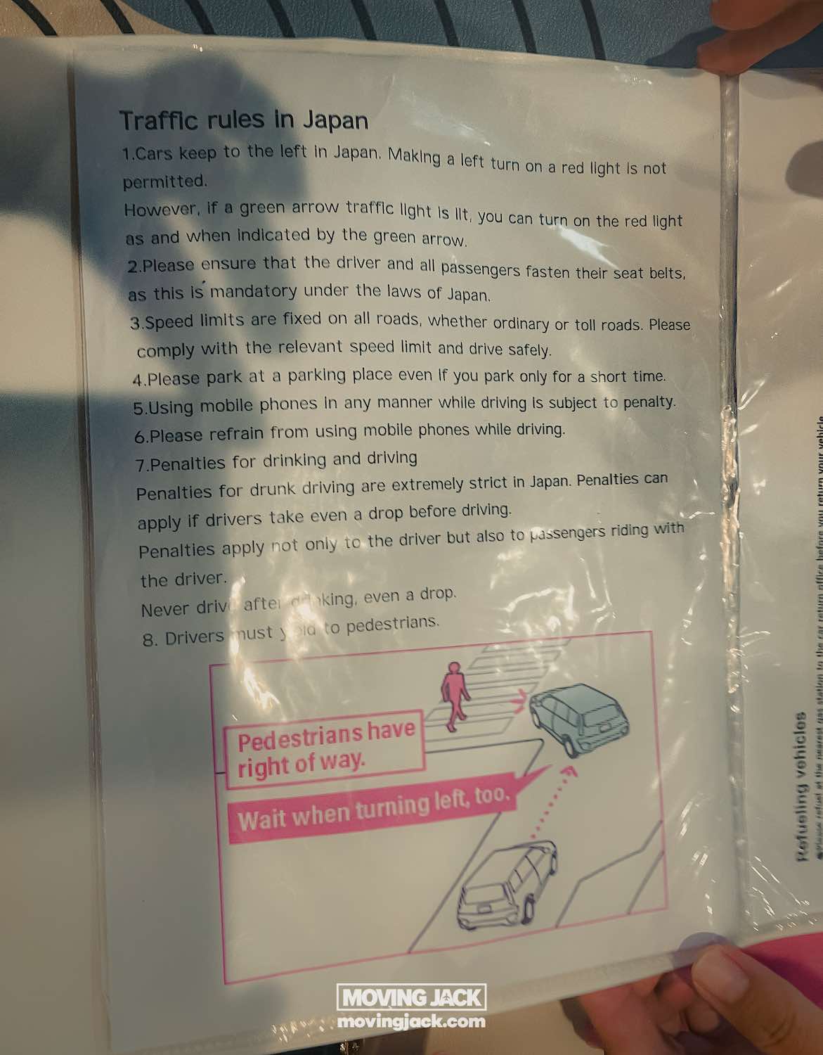 A laminated sheet with "traffic rules in japan" lists road rules, perfect for those renting a car in okinawa. Below, a diagram shows a car waiting for pedestrians before turning left, with pink text highlighting pedestrian priority. -copyright-moving-jack. Com
