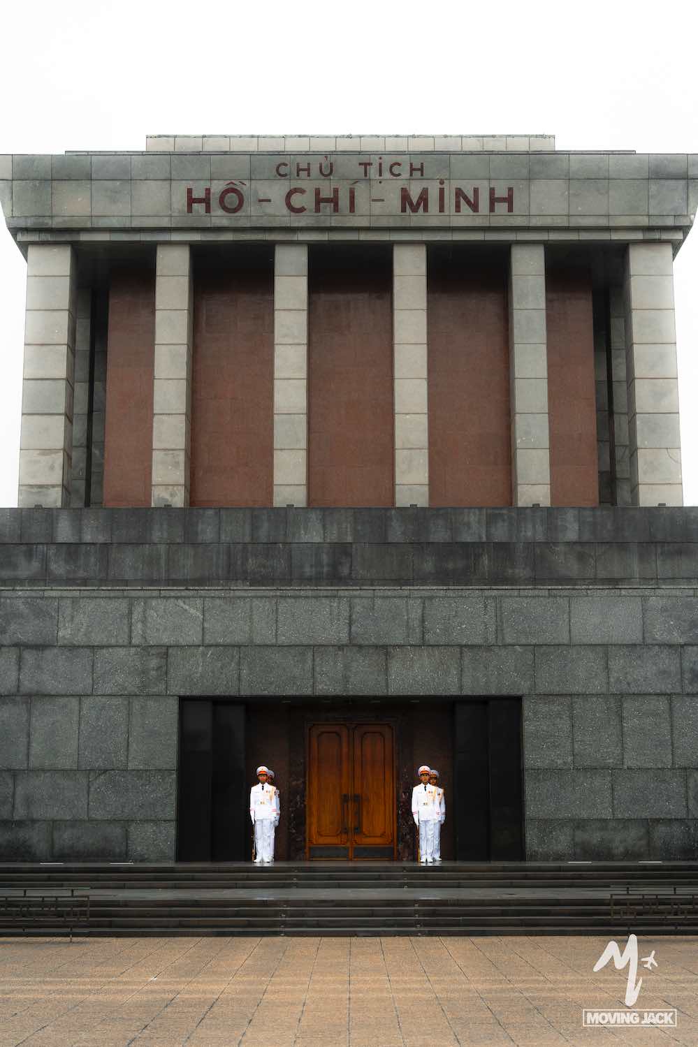 Twee bewakers in uniform staan bij de ingang van het Ho Chi Minh-mausoleum, een groot stenen gebouw met pilaren en Vietnamese inscripties boven de hoofdingangen. -Copyright-moving-jack.com