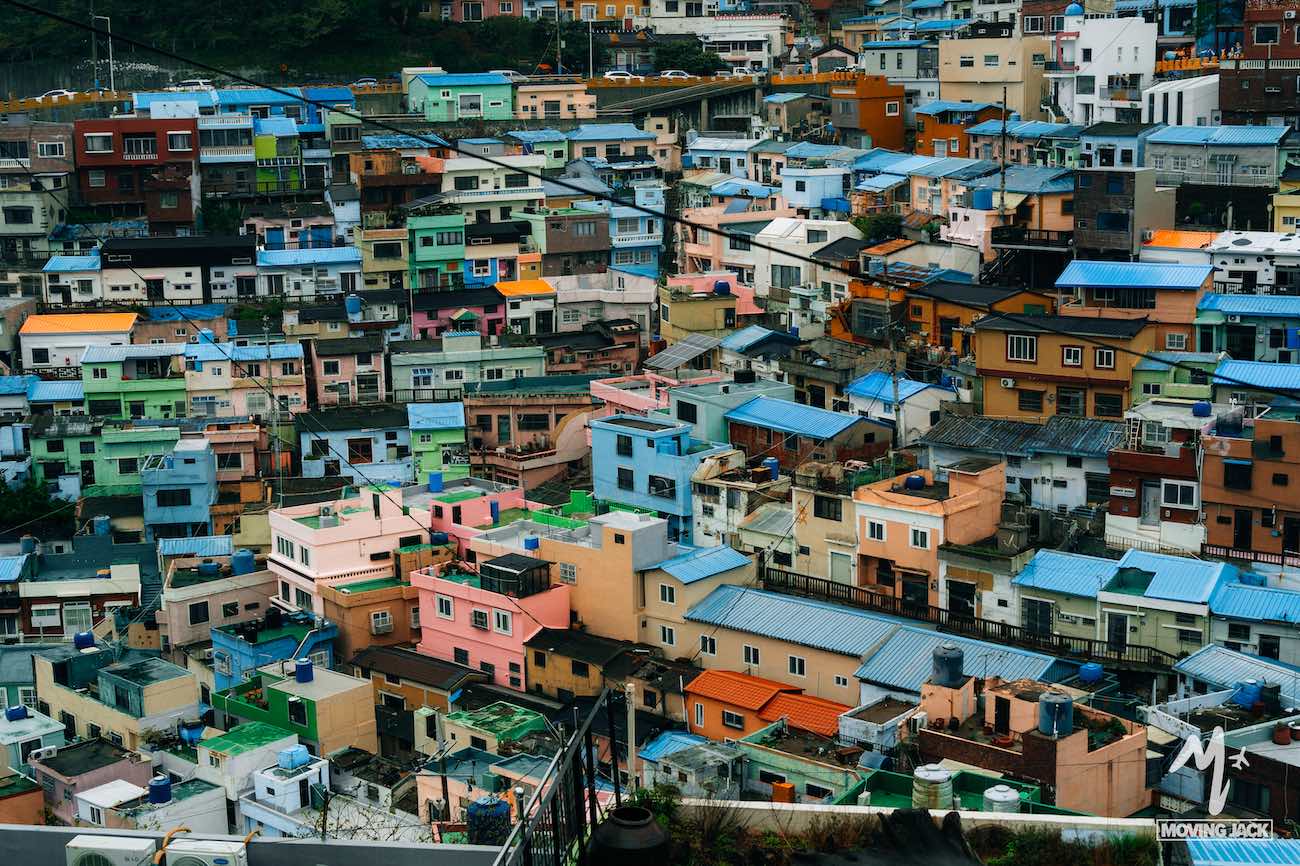 A dense hillside neighborhood filled with colorful houses, each with vibrant roofs and walls, showcases why many ask, "Is Busan worth visiting?" The vibrant scenery offers a unique charm you won’t find anywhere else.