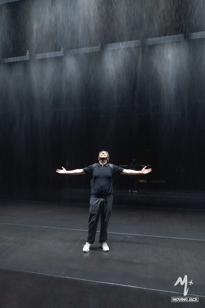 Person in black clothing stands on stage with arms outstretched, looking up as rain falls from above, evoking the dramatic energy that makes travelers wonder: is Busan worth visiting for moments like this?.