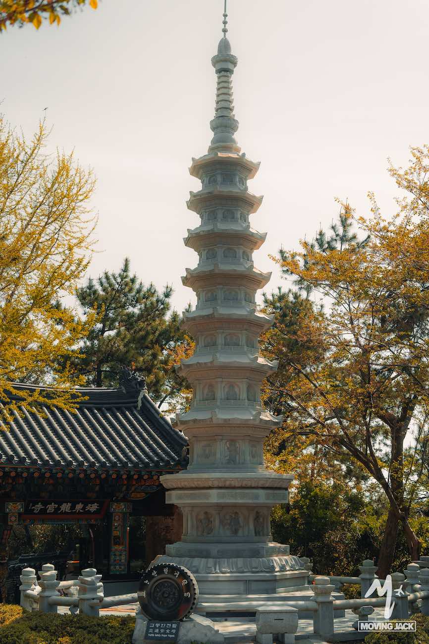 Tall white stone pagoda surrounded by trees with a traditional Korean building in the background—just one reason why many ask, is Busan worth visiting?.