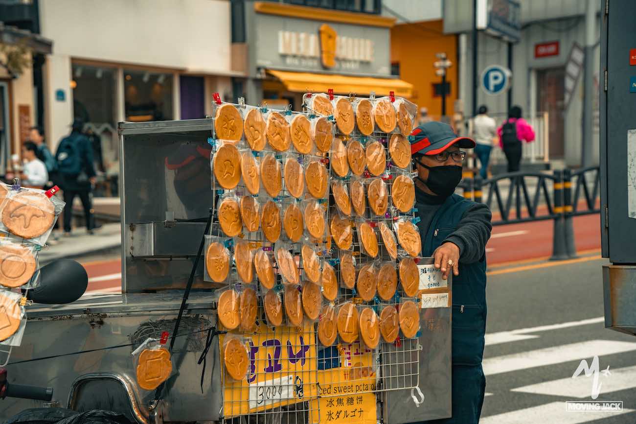 Street vendor selling dalgona candies from a cart in a lively city area—scenes like this make you wonder, is Busan worth visiting for its vibrant street life and local treats?.