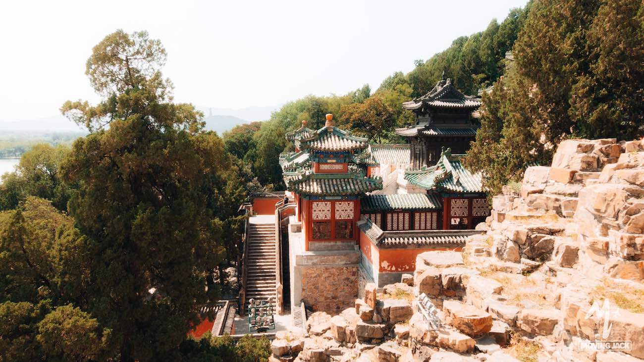 Traditionele Chinese architectuur met sierlijke groene pannendaken staat te midden van weelderige bomen en rotsachtig terrein, badend in warm zonlicht. Zulke taferelen doen je afvragen: is Shanghai een bezoek waard? De historische plekken bieden een glimp van tijdloze schoonheid. -Copyright-moving-jack.com