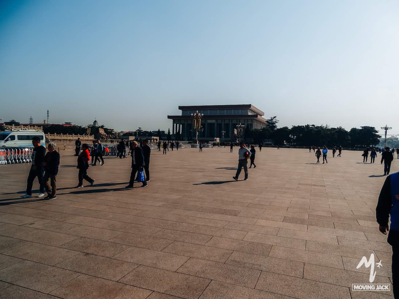 People walk across a large open square toward a rectangular building in the background under a clear blue sky, exploring the city and searching for where to stay in Beijing.