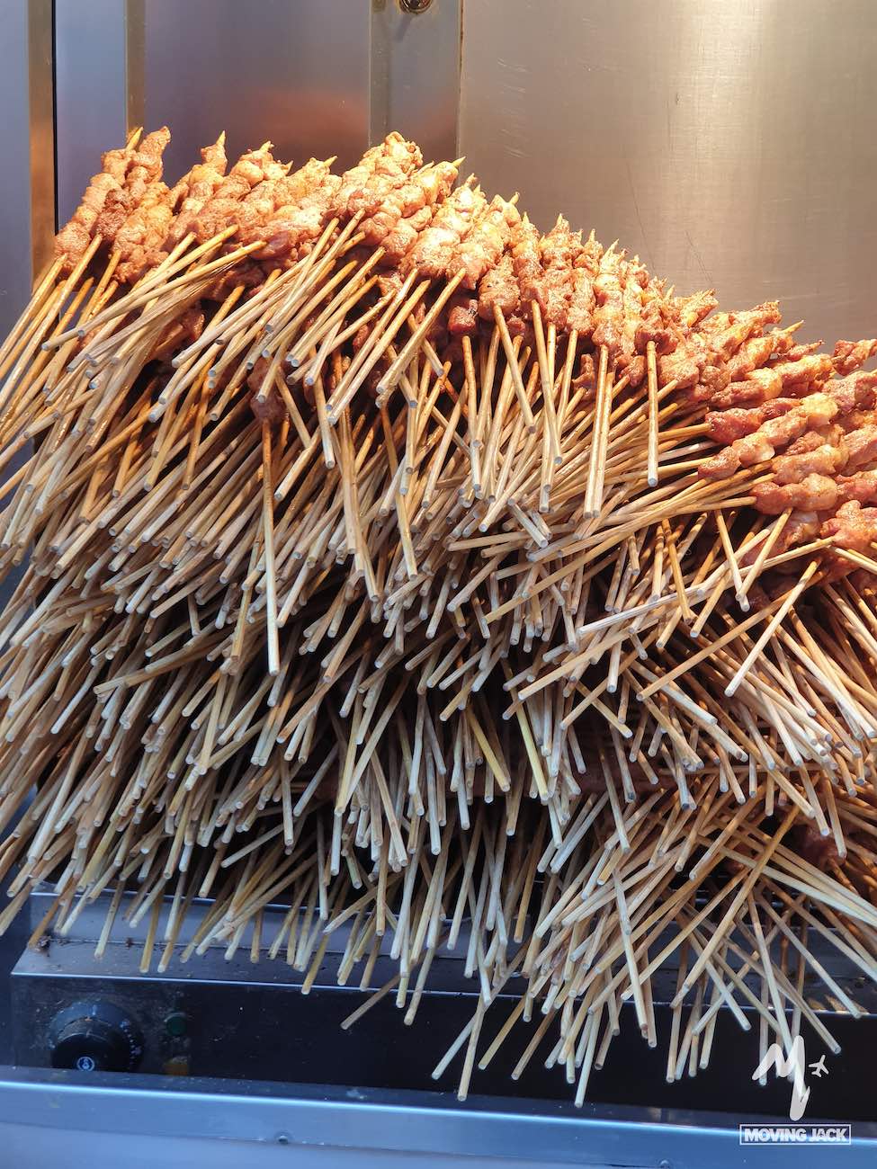 A large stack of grilled meat skewers arranged on a metal rack, the wooden sticks overlapping and pointing outward in various directions—perfect fuel after a day spent exploring where to stay in Beijing.