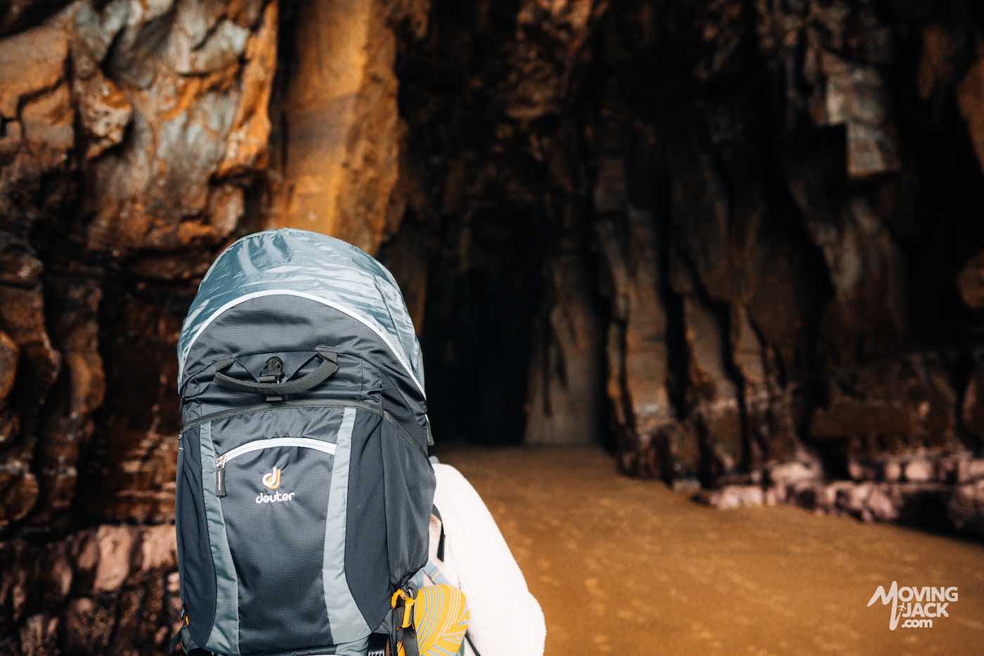 Een persoon met een grote rugzak staat bij de ingang van een donkere, rotsachtige grot en vraagt zich af: "Zijn de Kathedraalgrotten de moeite waard om te bezoeken?" De mysterieuze sfeer nodigt uit tot verkenning en avontuur.
