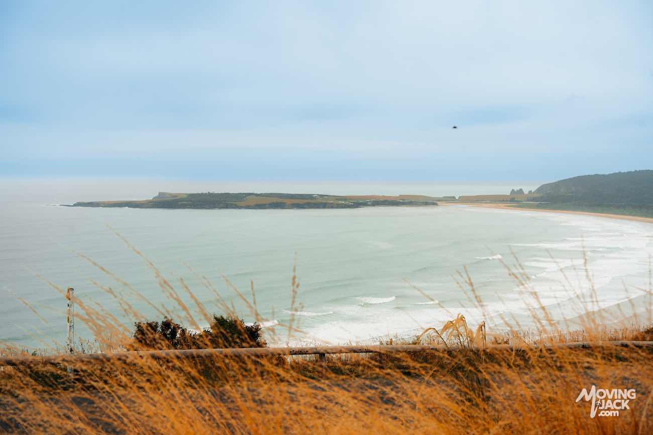 Uitzicht op een baai aan de kust met golven en een grasveld op de voorgrond onder een bewolkte hemel, landtongen in de verte – bij dit tafereel vraag je je af: zijn de Cathedral Caves de moeite waard om te bezoeken voor zulke bezienswaardigheden?.