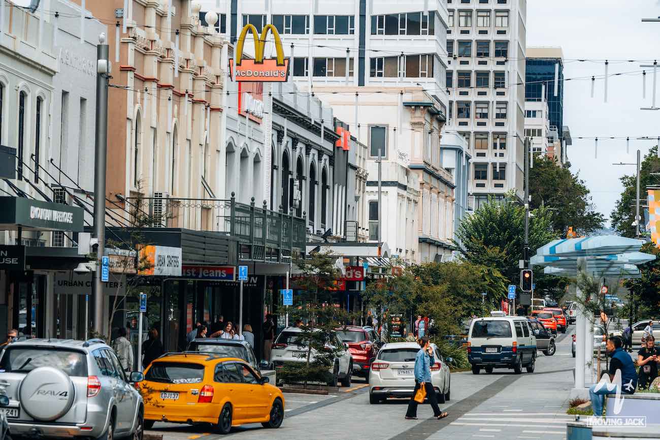 Busy city street with cars, pedestrians, shops, and a McDonald's sign among tall buildings—making you wonder if exploring somewhere quieter like New Zealand by campervan is worth it.