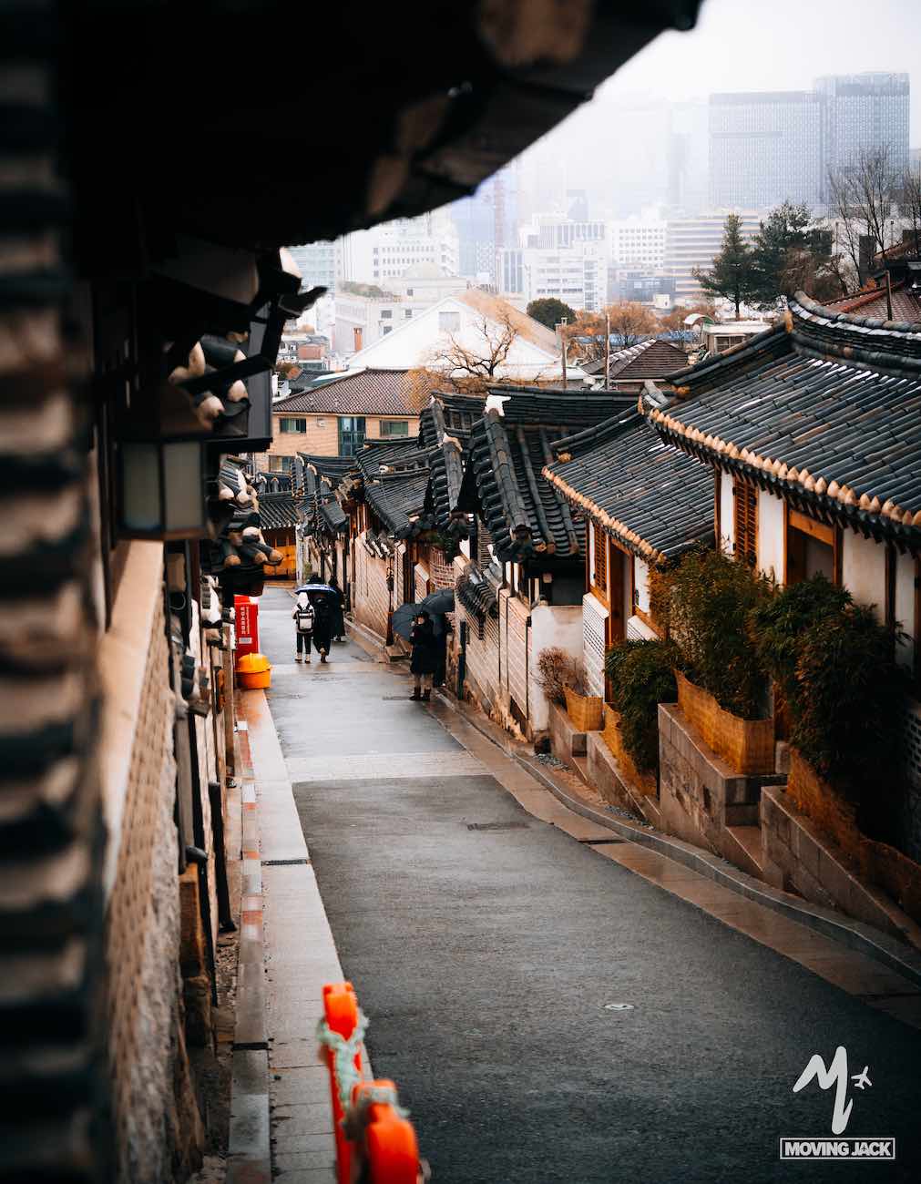 Een smalle straat met traditionele Koreaanse huizen, voorbijgangers en moderne gebouwen op de achtergrond – een absolute aanrader voor iedereen die Seoul bezoekt.