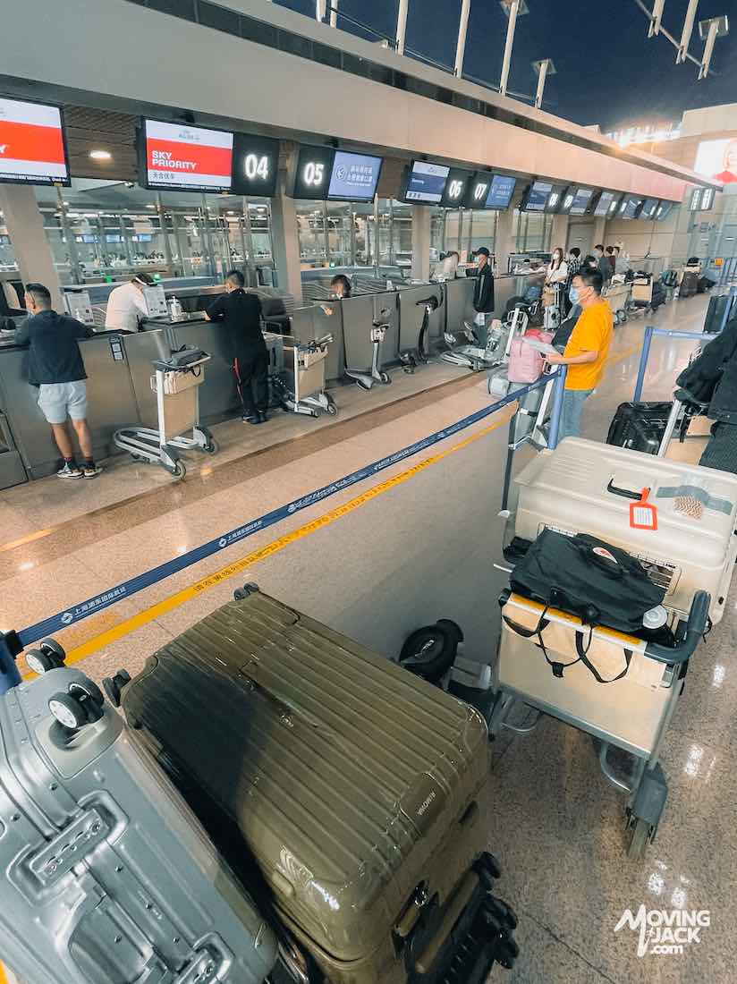 Travelers line up with luggage at an airport check-in counter at one of the bustling Shanghai airports; suitcases are stacked in the foreground.