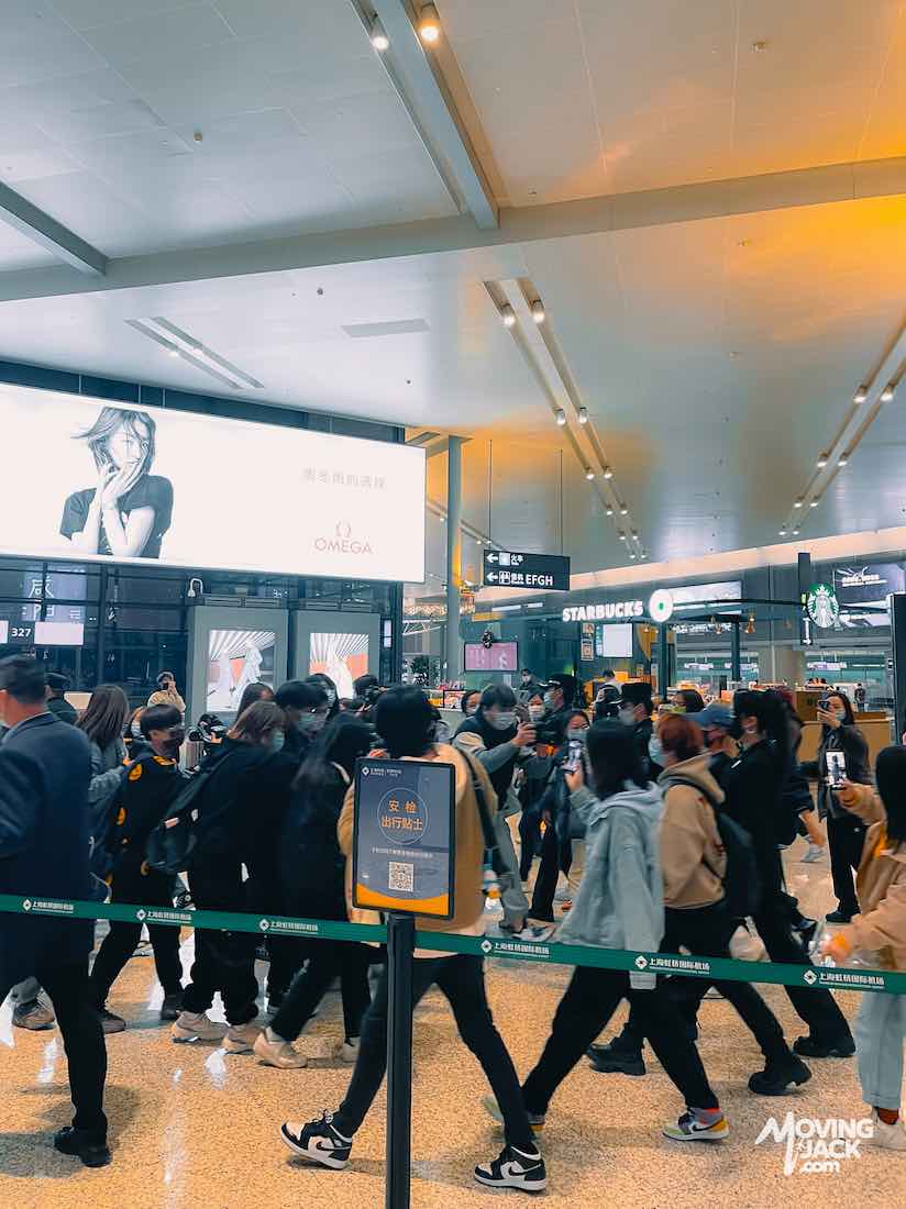 Crowd of people walking inside a shanghai airports terminal with Starbucks and Omega signs visible.