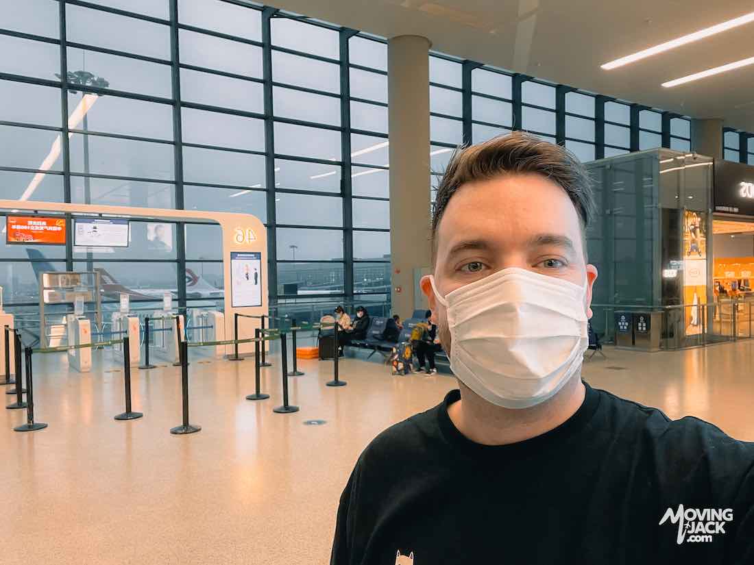 Man wearing a face mask takes a selfie inside a modern shanghai airports terminal with large windows and spacious waiting area.