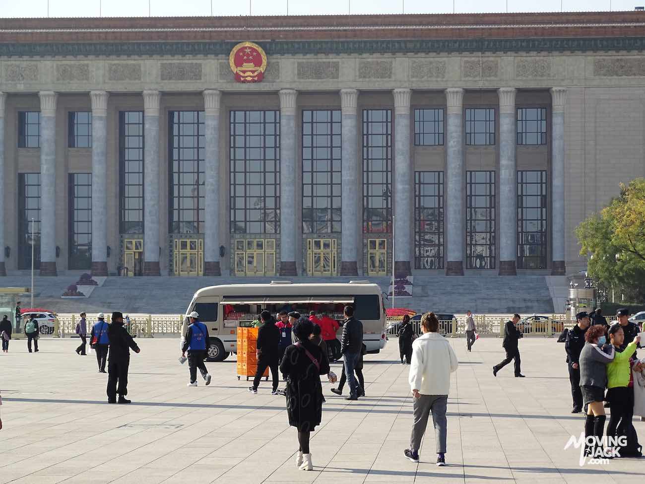 People walk and gather in front of a large government building in China.