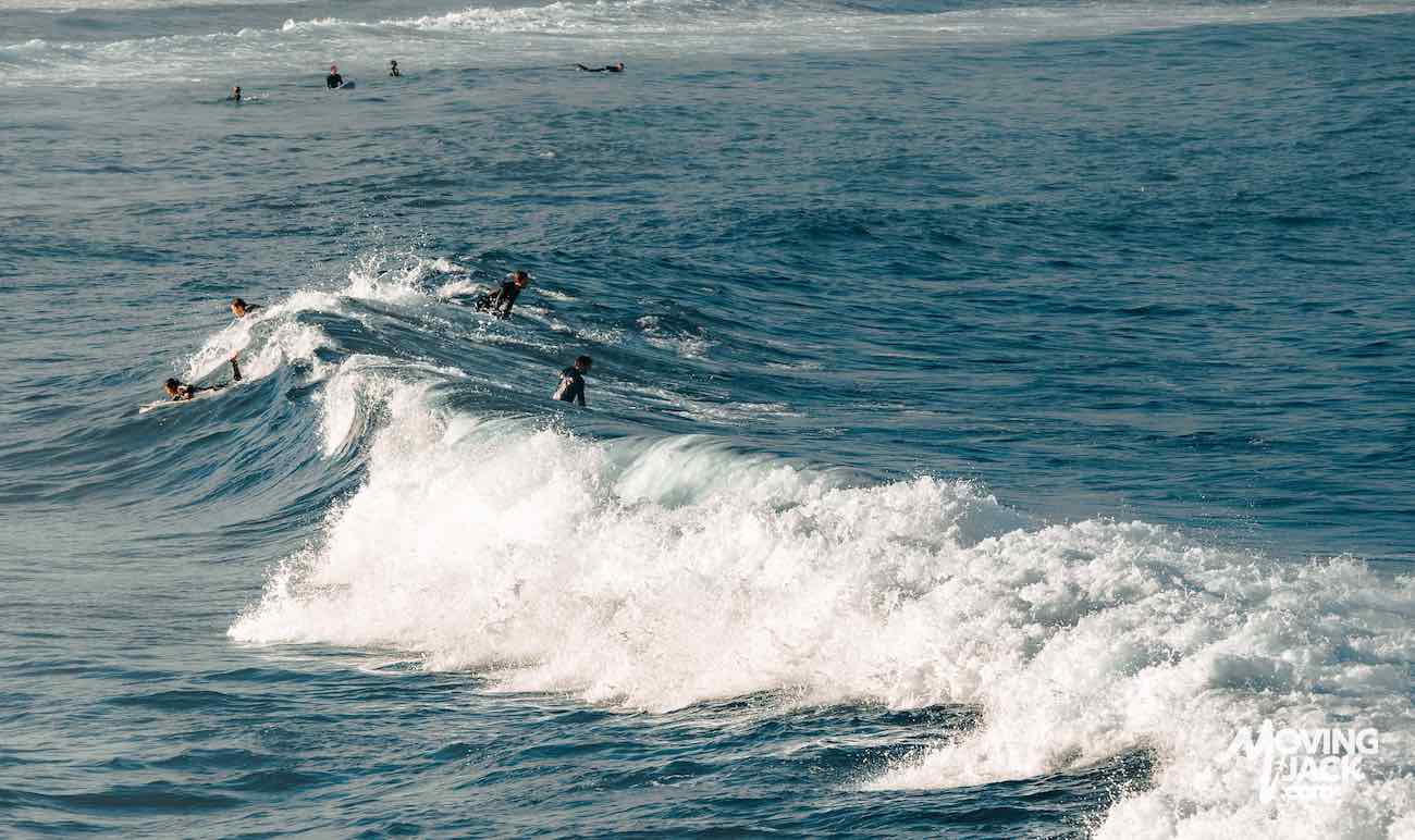 Surfers riding and waiting for waves in the ocean on a sunny day; white foam visible on the waves—perfect inspiration for those searching where to stay in Sydney near the best beaches.