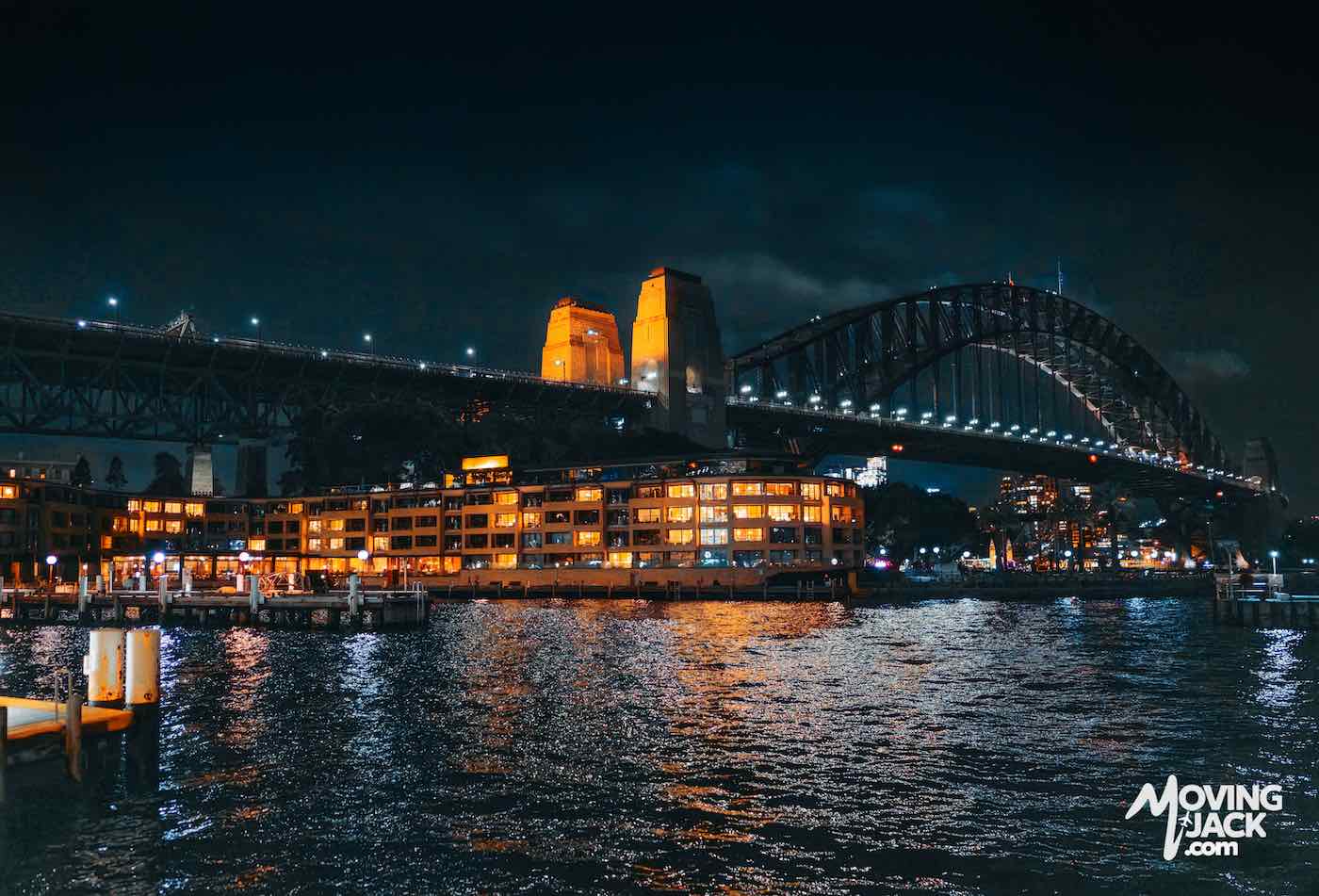 Sydney Harbour Bridge at night with illuminated buildings reflected in the water; perfect inspiration for finding where to stay in Sydney.