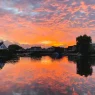 20 photos: stunning skies in the netherlands (zeeland) 31 sony a7c camera,travel camera,a7c street photography Sunset over a calm lake with silhouetted houses and trees reflects vibrant orange and pink clouds, capturing the stunning skies in the netherlands.